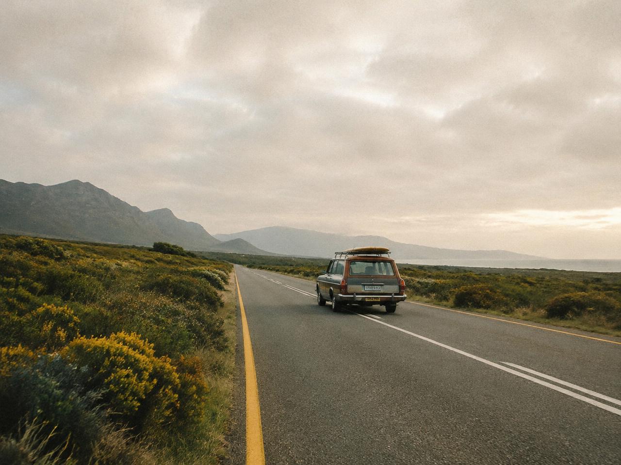 Old station wagon with a surfboard on an empty West Coast road
